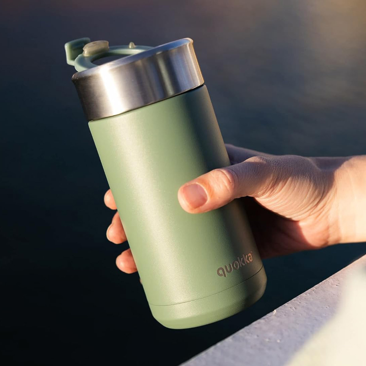 Una mano tiene un bicchiere verde opaco con coperchio argentato.