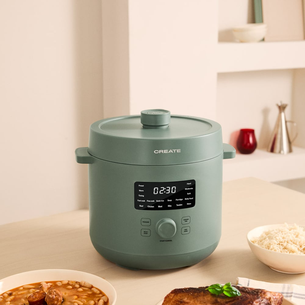 Una olla a presión verde con pantalla digital en una mesa junto a comida.