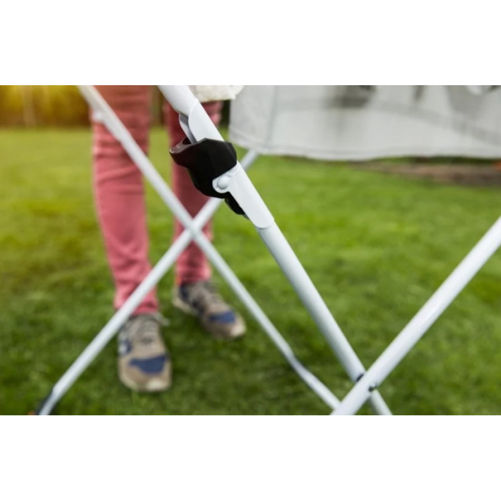 Osoba w różowych spodniach i tenisówkach obok białej suszarki na trawie.