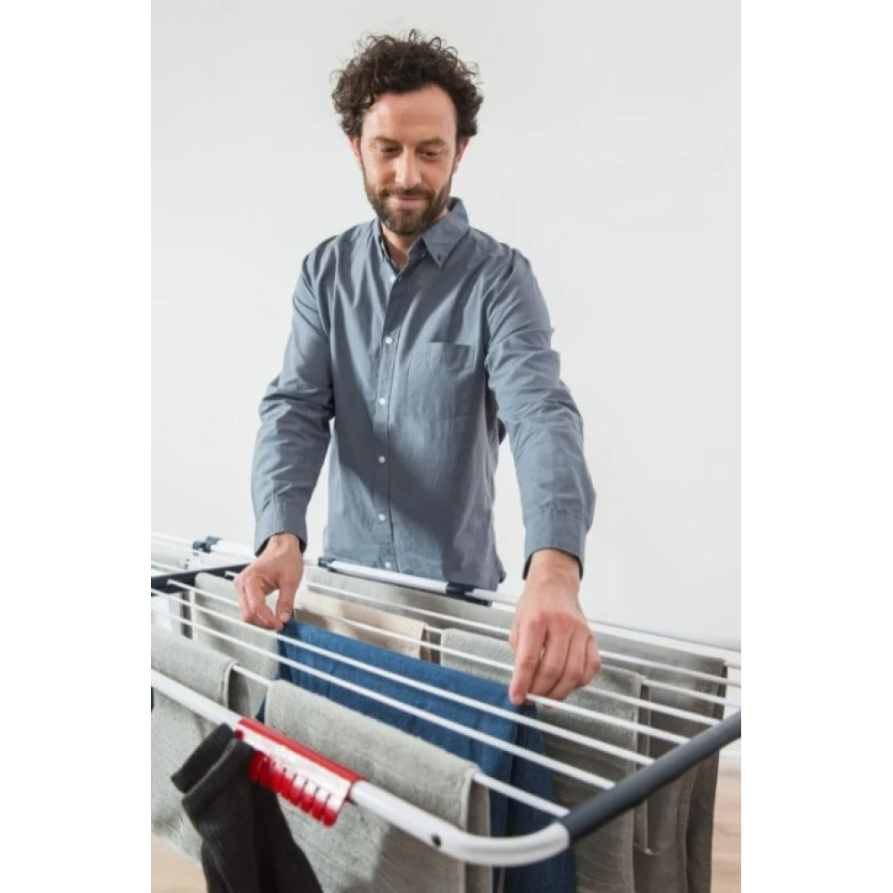 Mężczyzna z kręconymi włosami wiesza pranie na suszarce.