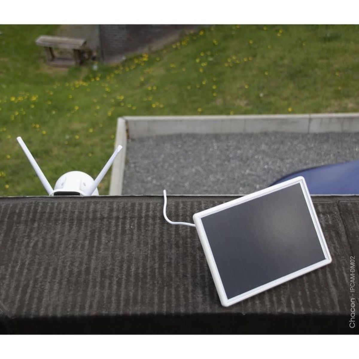 Een witte wifi-camera met antennes en zonnepaneel op een donker dak.