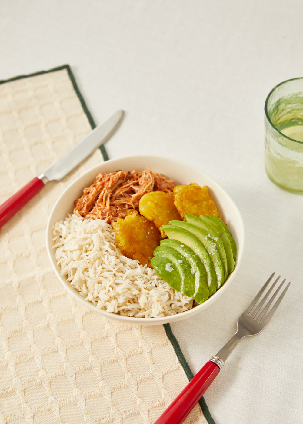 Bol de arroz con pollo deshebrado, plátanos y aguacate. Mesa puesta.