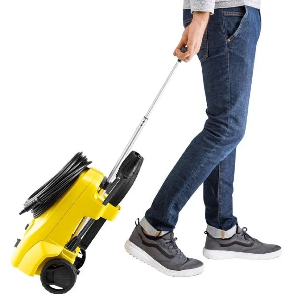 Osoba w dżinsach ciągnie żółtą myjkę ciśnieniową z teleskopowym uchwytem.