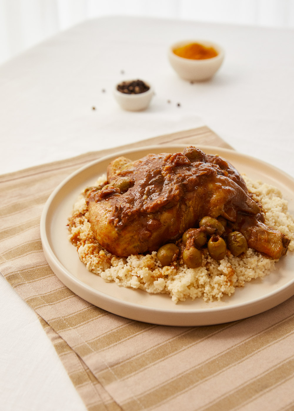 Un muslo de pollo con aceitunas y salsa sobre cuscús, servido en un plato.