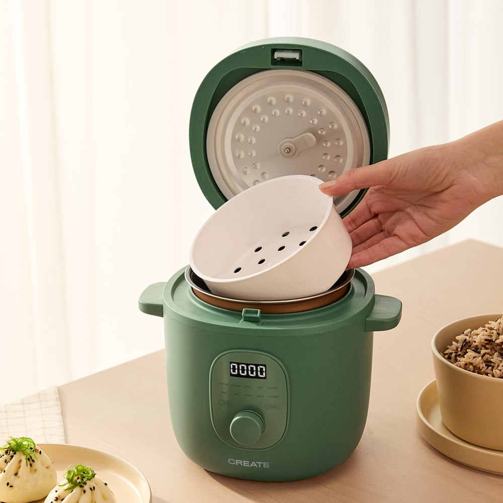 Olla arrocera verde con tapa abierta, una mano coloca una cesta de vapor blanca.