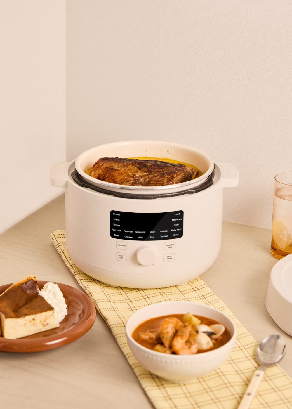 Una olla eléctrica blanca contiene un asado cocido. Al lado hay tarta de queso y estofado de camarones.