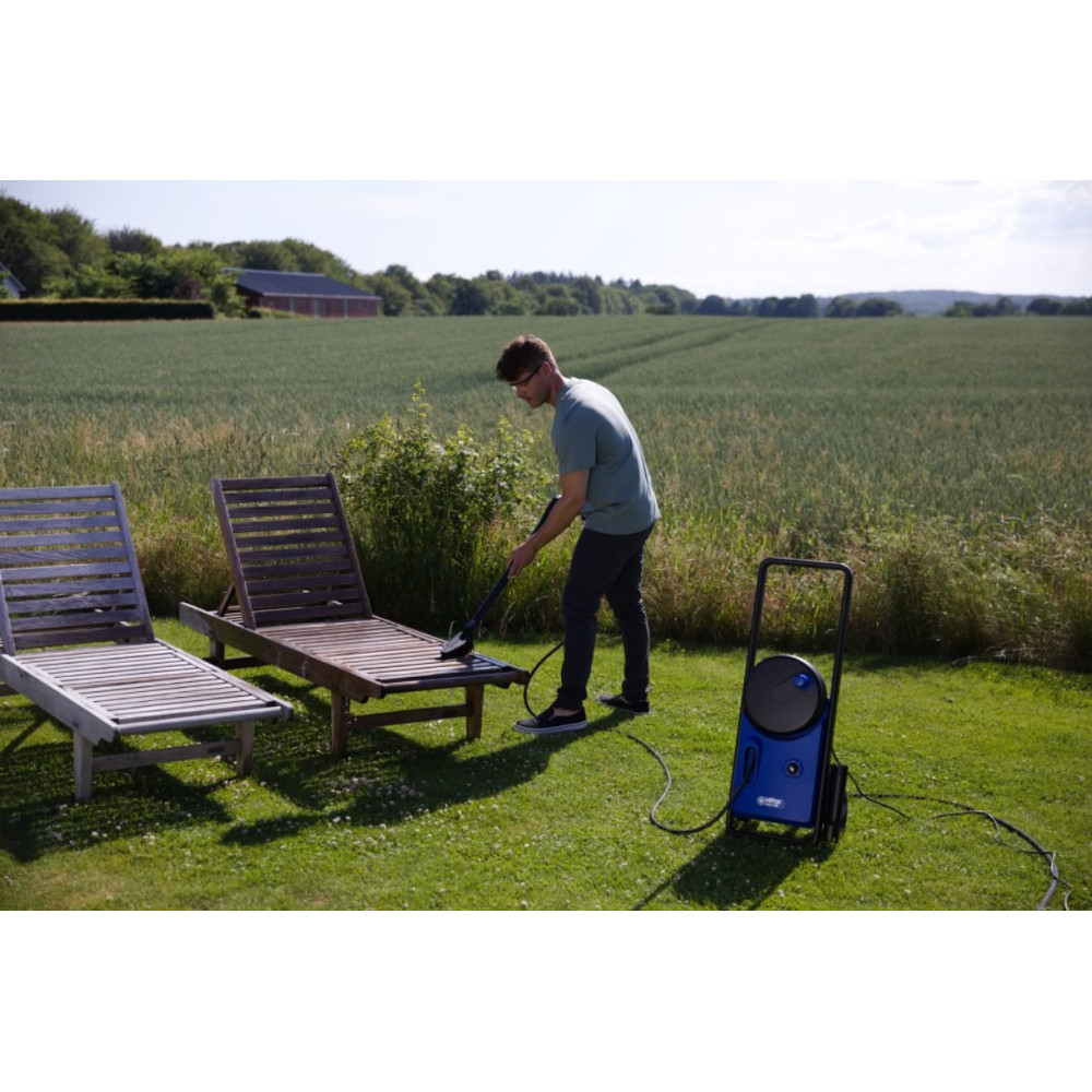 Mężczyzna myje leżak ciśnieniowo na trawiastym podwórzu.