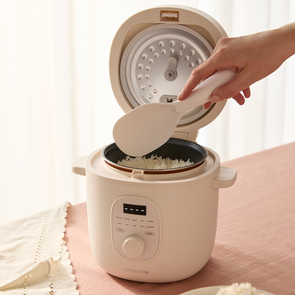 Una mano usa una pala para arroz para sacar arroz cocido de una arrocera.