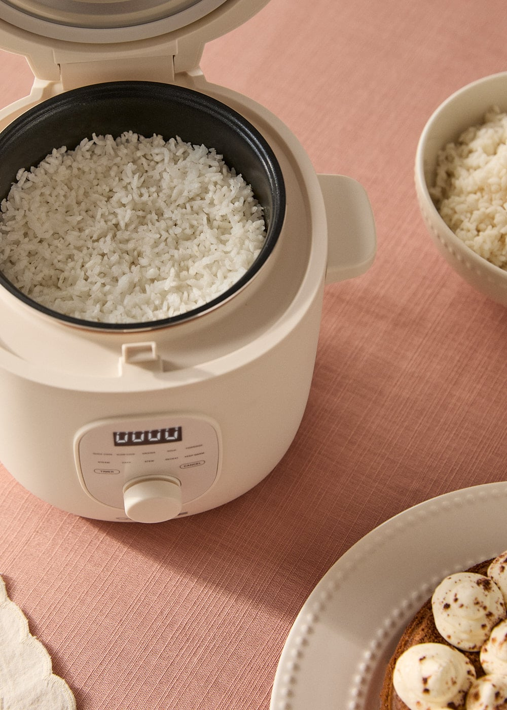 Una arrocera abierta con arroz cocido y un cuenco de arroz al lado.