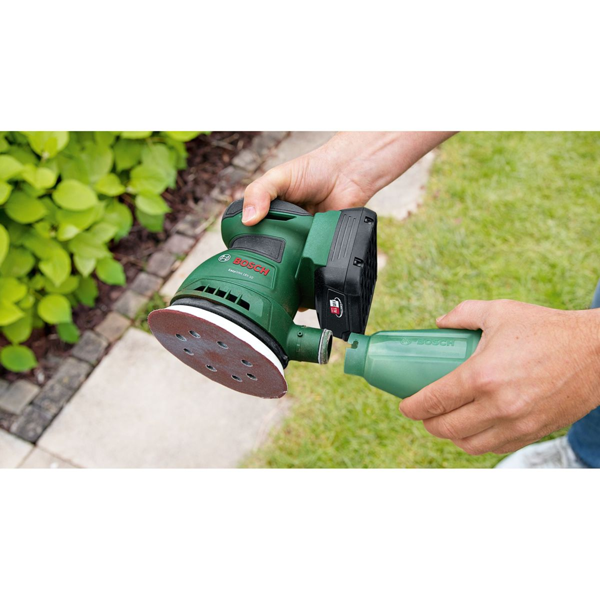 Eine grüne Bosch Schleifmaschine mit Staubfangbehälter im Garten.