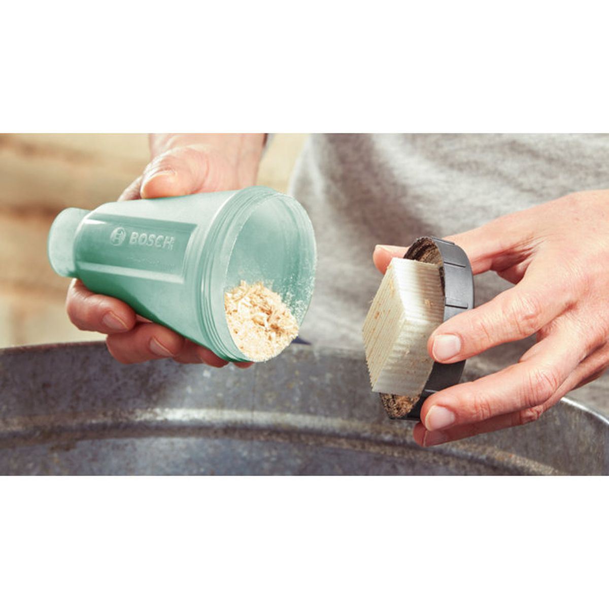 Hände halten einen grünen Bosch Behälter mit Pulver und eine Bürste mit Borsten.