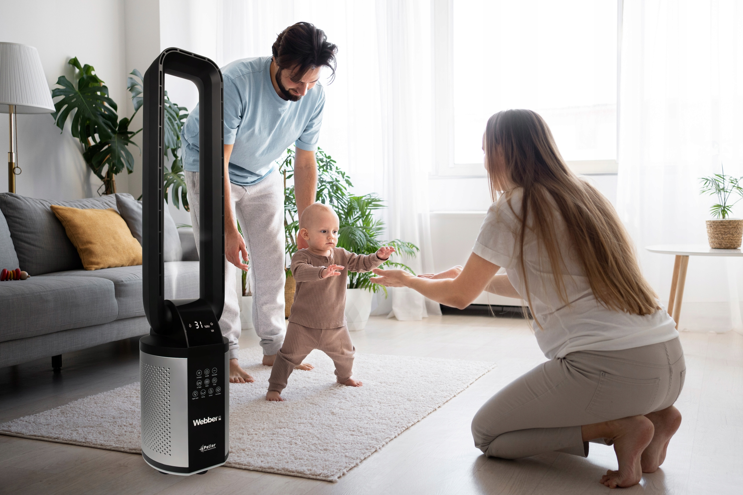 Familie mit Baby spielt vor einem Turmventilator in einem hellen Wohnzimmer.