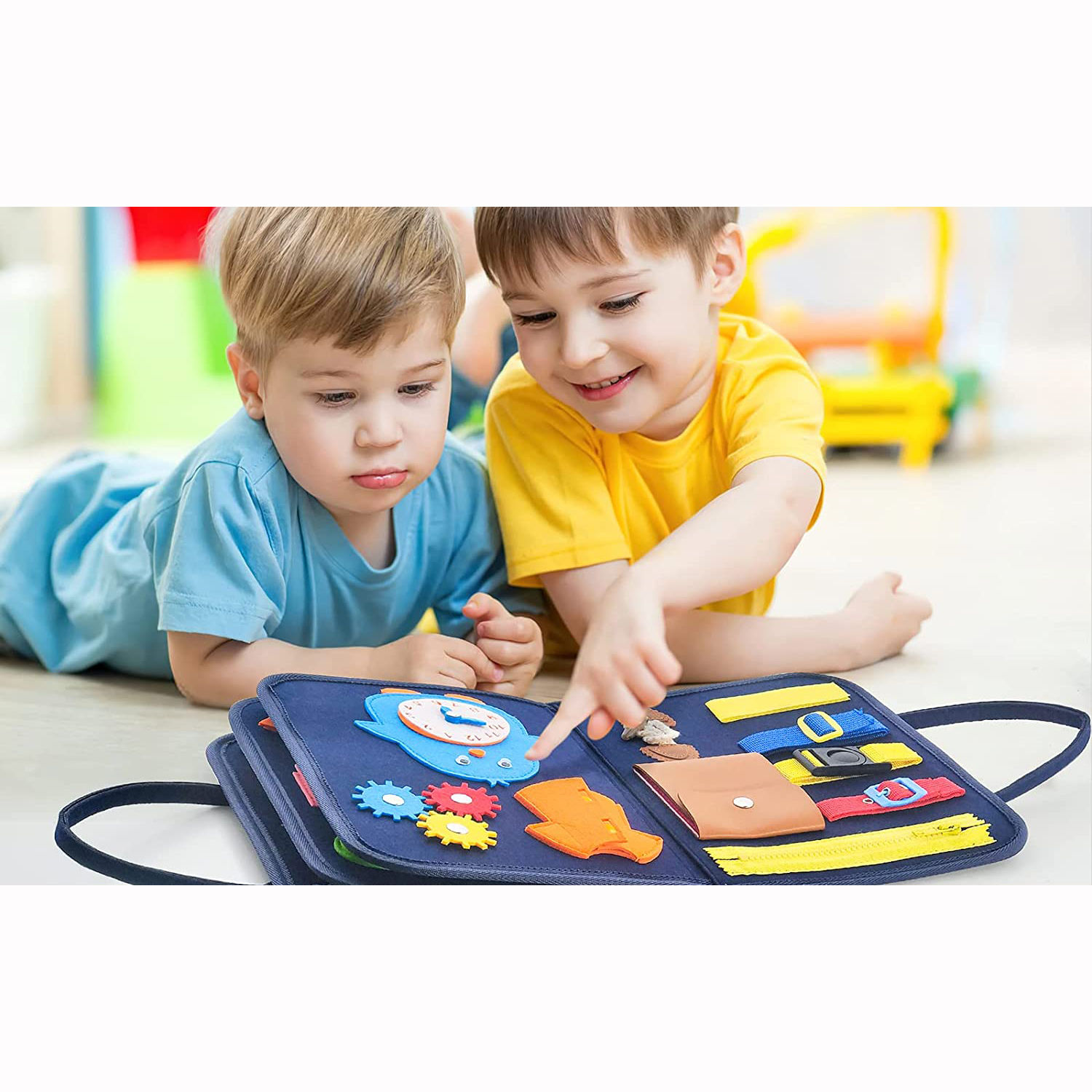 Zwei Jungen liegen auf dem Boden und spielen mit einem blauen Stoffbuch mit Schnallen und Zähnen.