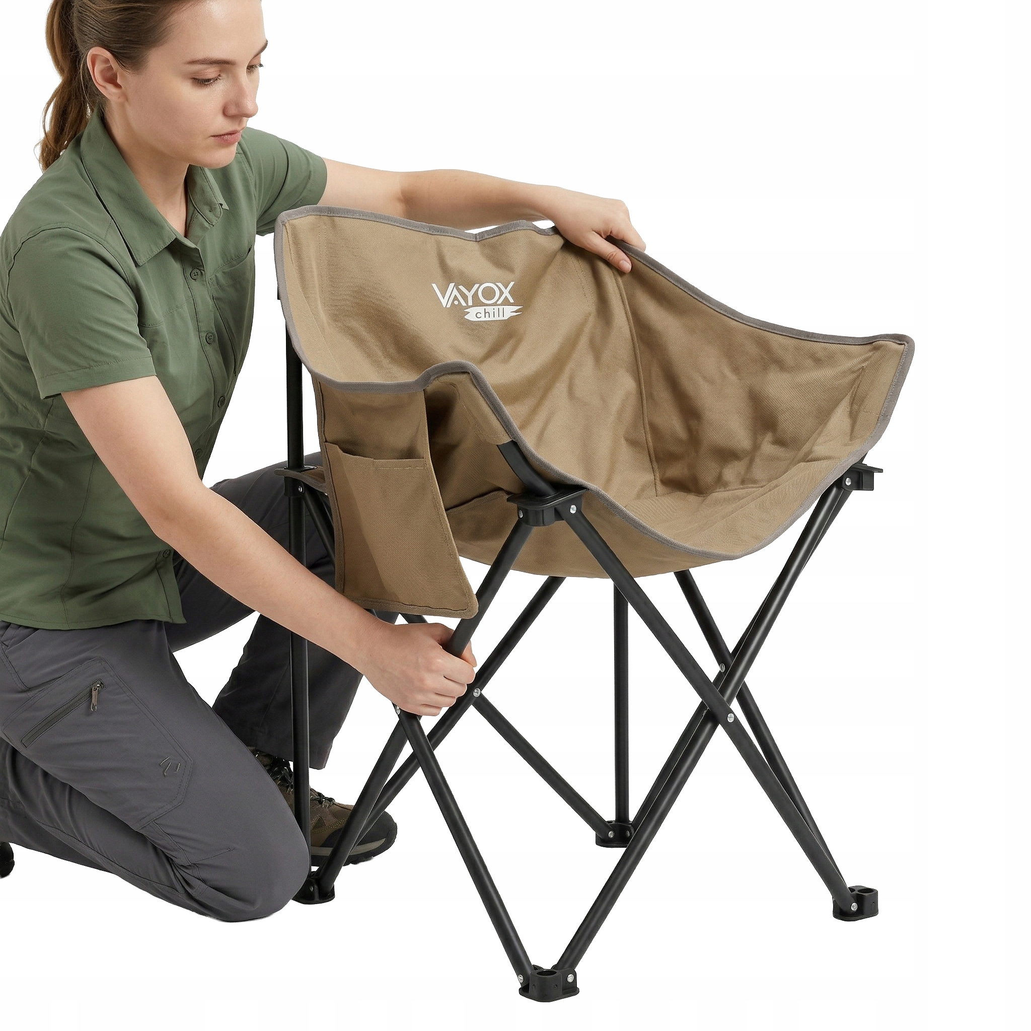 Kobieta w zielonym i szarym rozkłada brązowe krzesło kempingowe z kieszeniami.