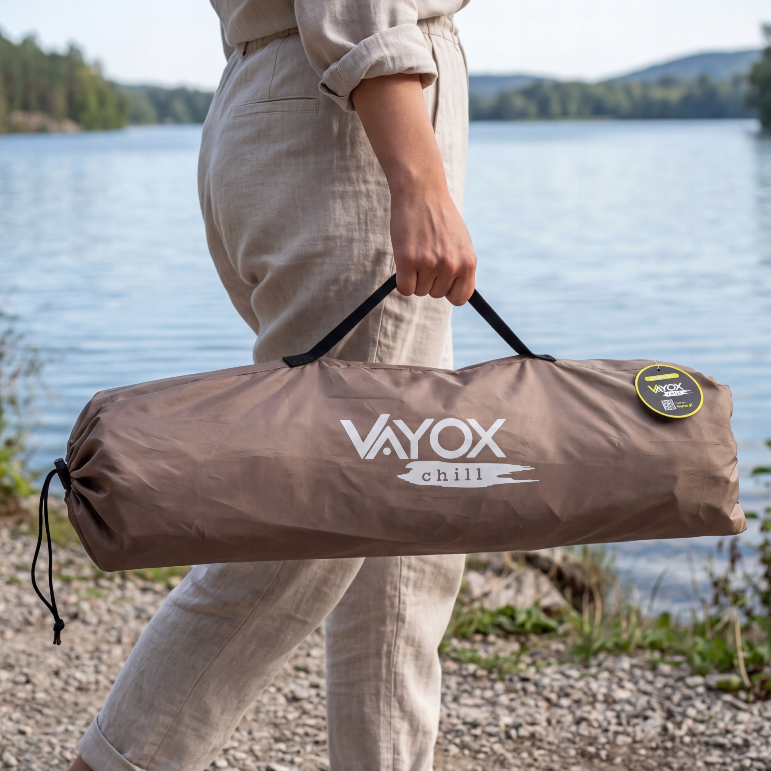 Osoba niesie brązową torbę z logo VAYOX CHILL nad jeziorem.