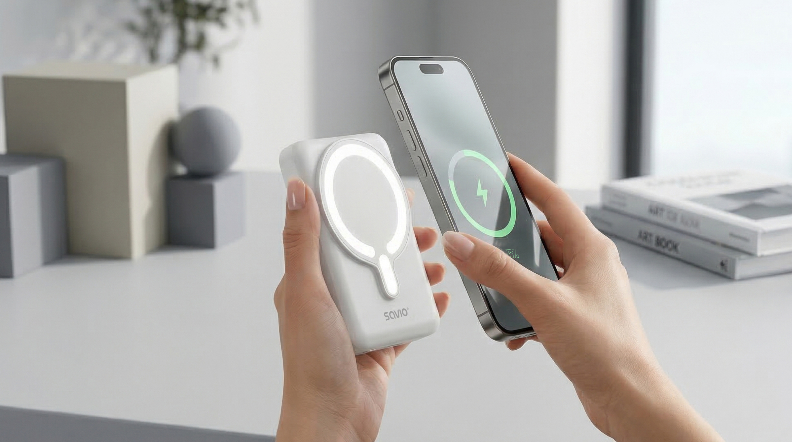 Dłonie trzymają białą magnetyczną powerbankę i smartfon z ikoną ładowania.