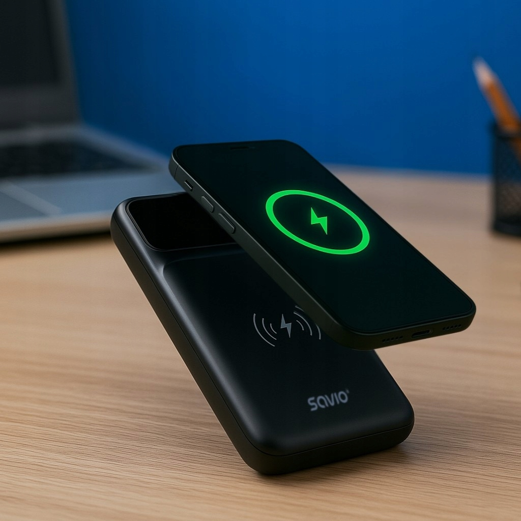 Czarny smartfon ładuje się bezprzewodowo na czarnym powerbanku na drewnianym biurku.