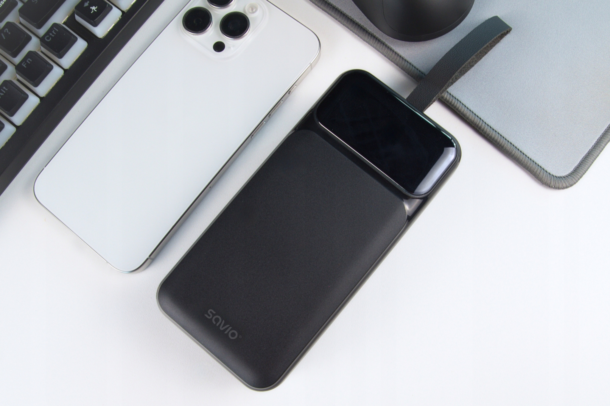 Biały smartfon, czarny power bank i klawiatura leżą na biurku.