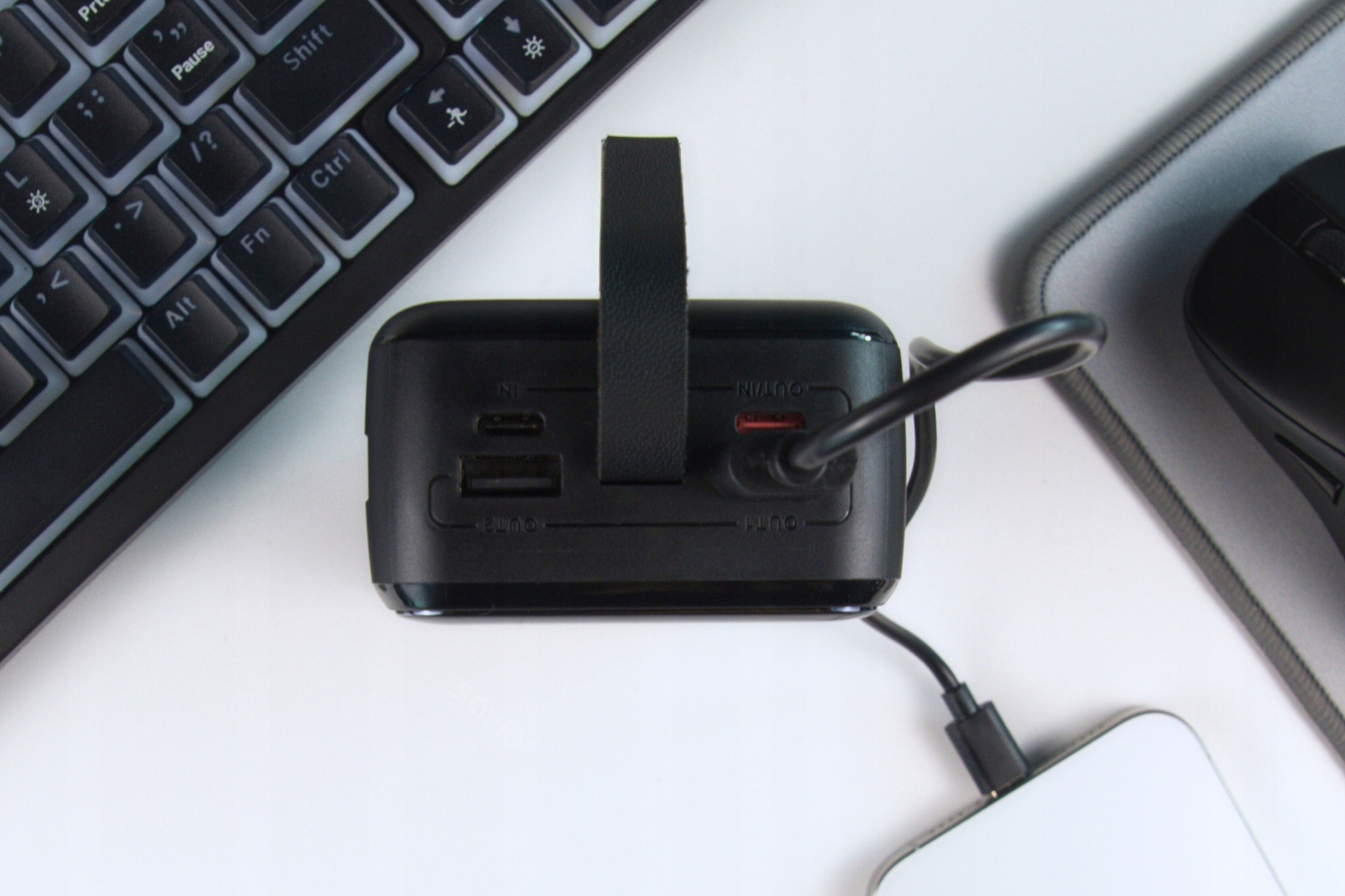 Czarny power bank podłączony do telefonu, obok klawiatury i myszy.