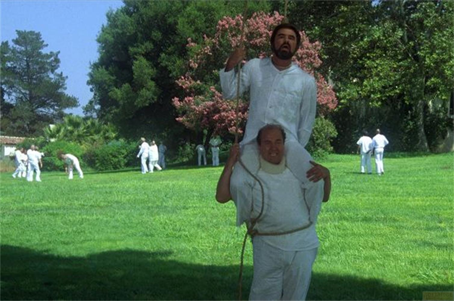 Uomo porta uomo sulle spalle all'aperto; diverse persone sullo sfondo.