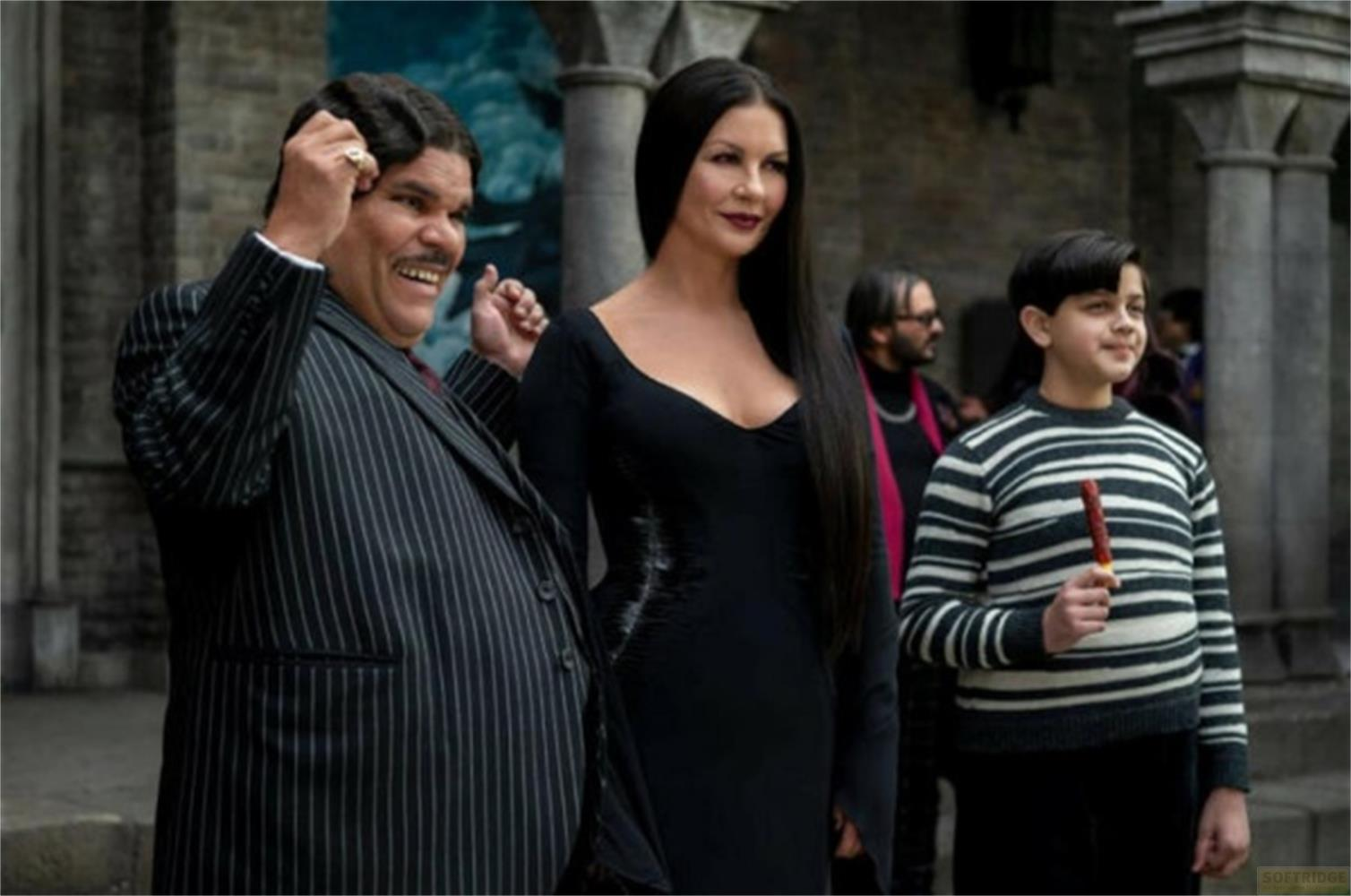 Gomez, Morticia und Pugsley Addams stehen in einem Gebäude vor einer Wand.