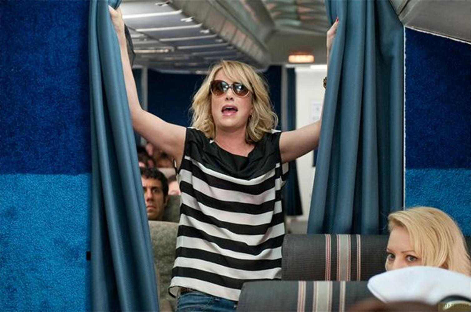 Donna in aereo con top a righe e occhiali da sole apre le tende.