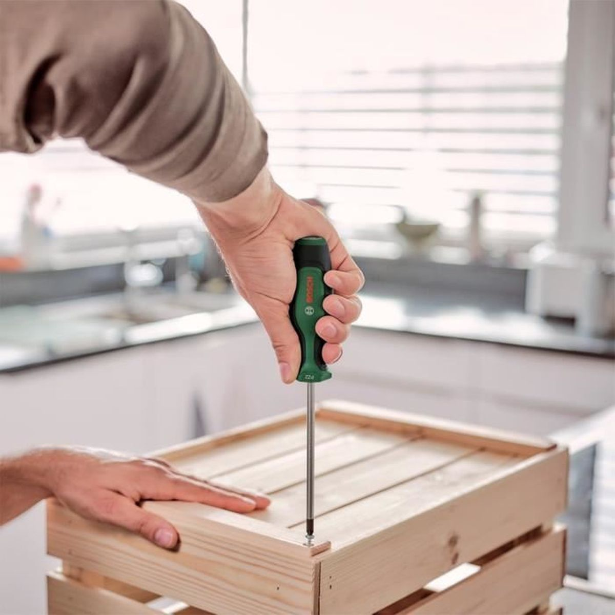 Mann schraubt mit Bosch-Schraubendreher an Holzkiste.