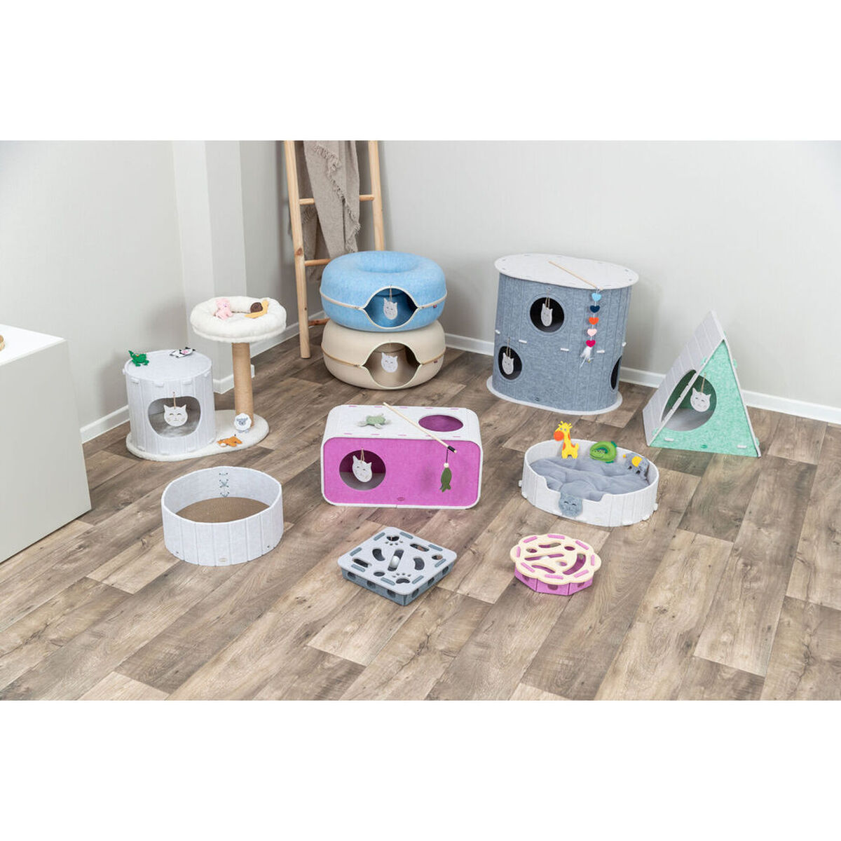 Mehrere bunte Katzenmöbel, darunter Türme, Höhlen und Spielzeuge, sind auf einem Holzboden angeordnet.