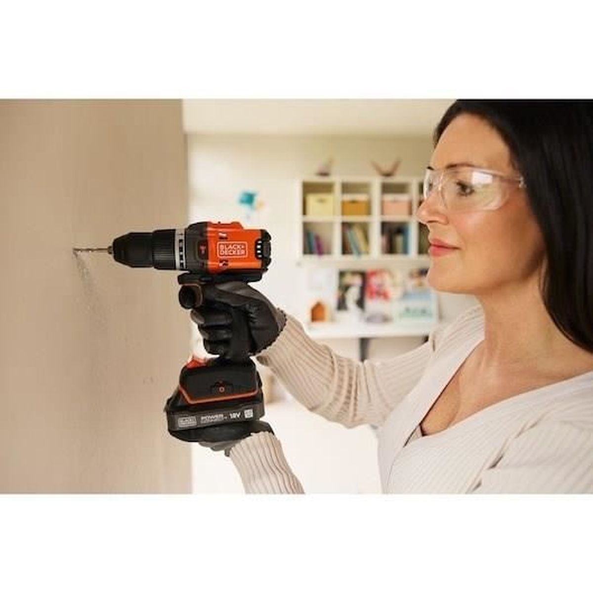 Eine Frau mit Schutzbrille bohrt mit einem orangefarbenen Bohrer in eine Wand.