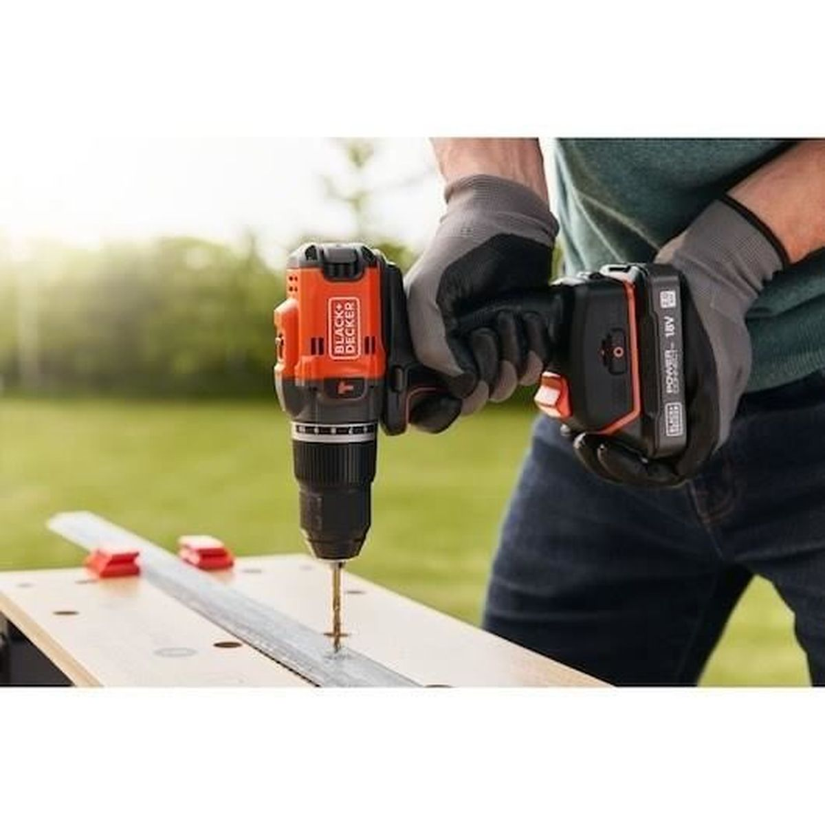 Person bohrt mit Akku-Bohrschrauber in Holz. Grau-schwarze Handschuhe, orange-schwarzer Bohrer.