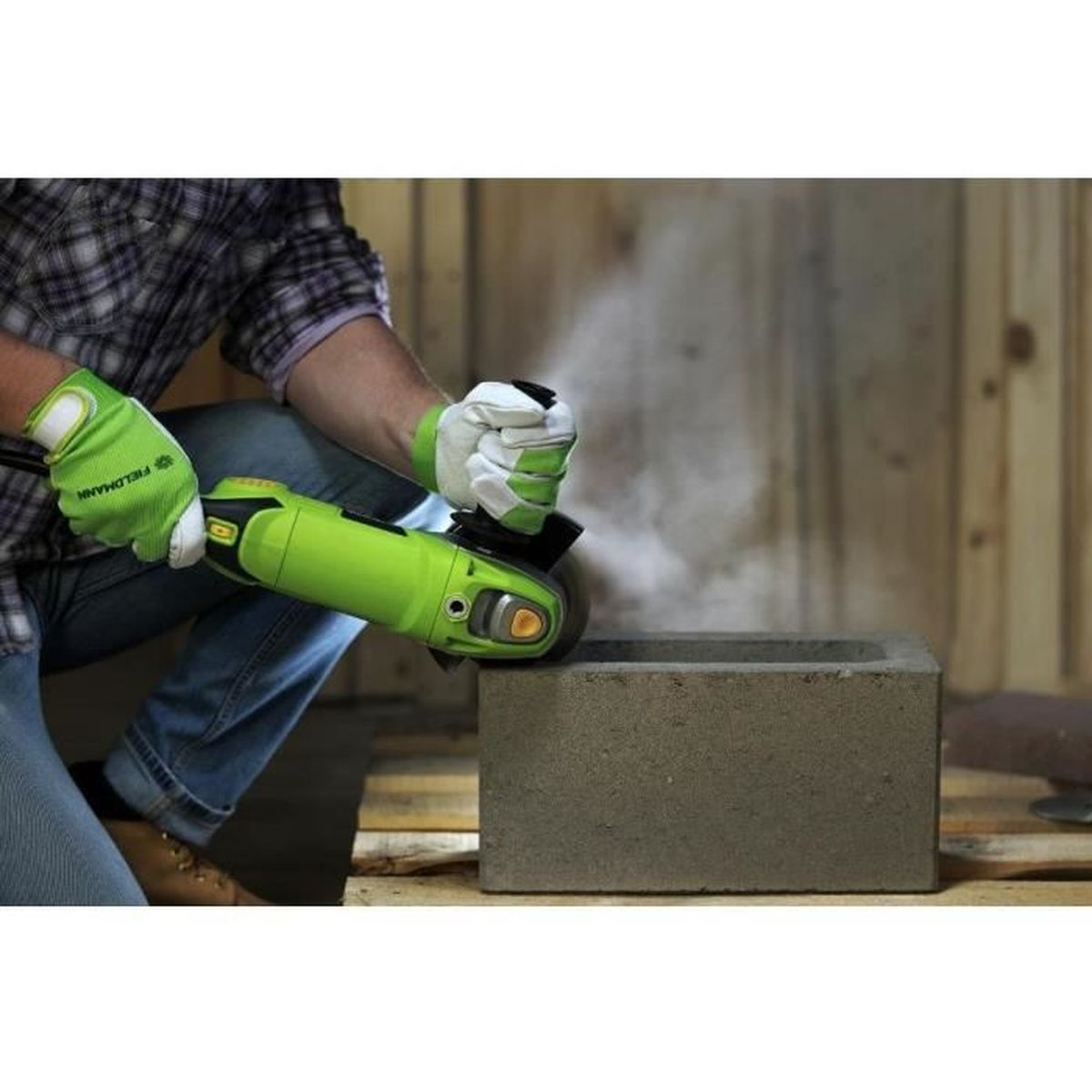 Osoba w zielonych rękawicach szlifuje blok betonu szlifierką kątową.