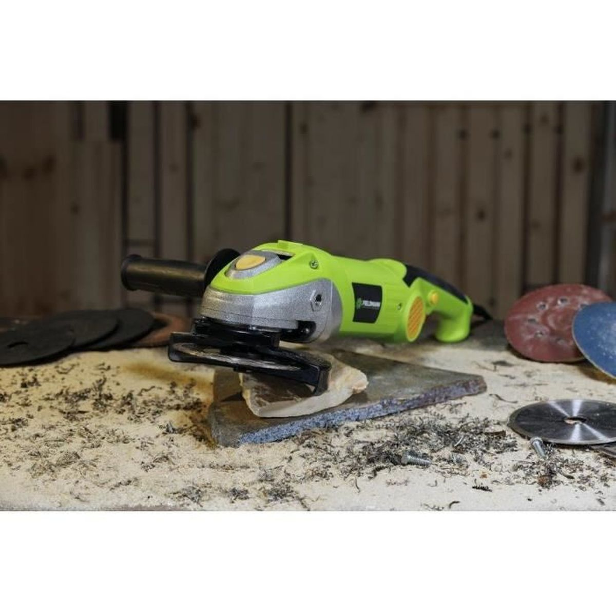 Zielona szlifierka kątowa leży na kamieniu, otoczona papierem ściernym i wiórami.