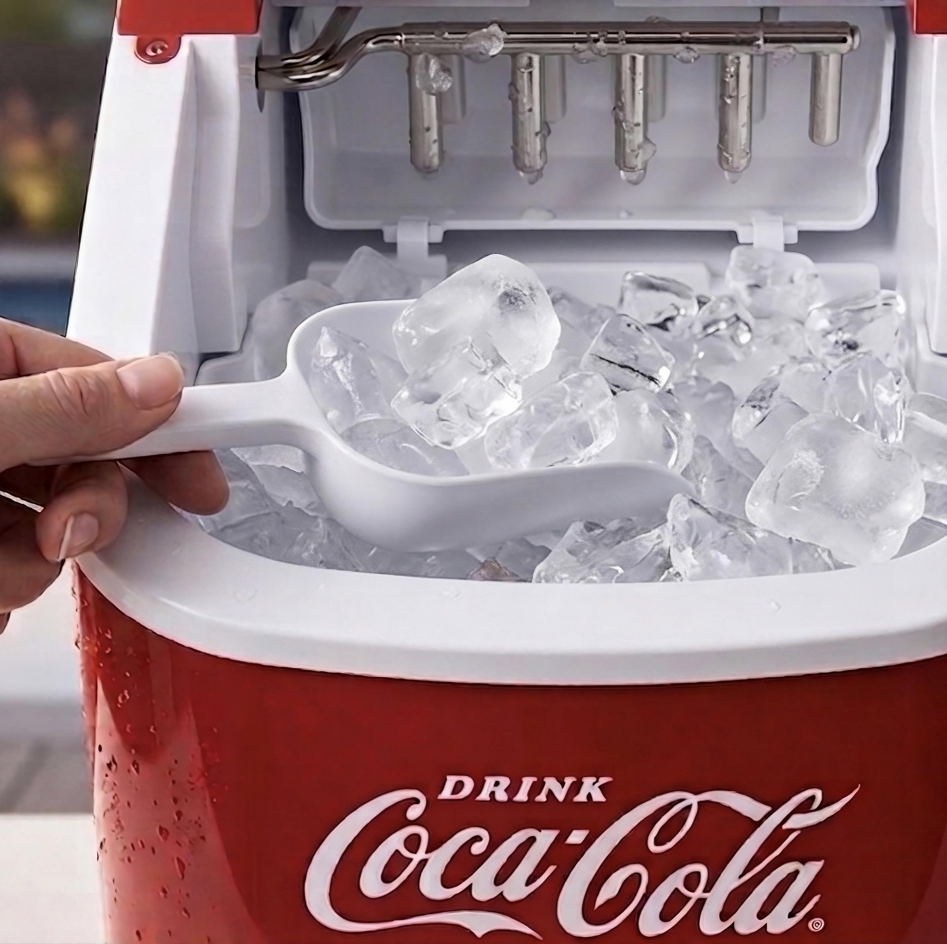Eine Hand schöpft Eiswürfel mit einer weißen Schaufel aus einem roten Coca-Cola-Eisbereiter.