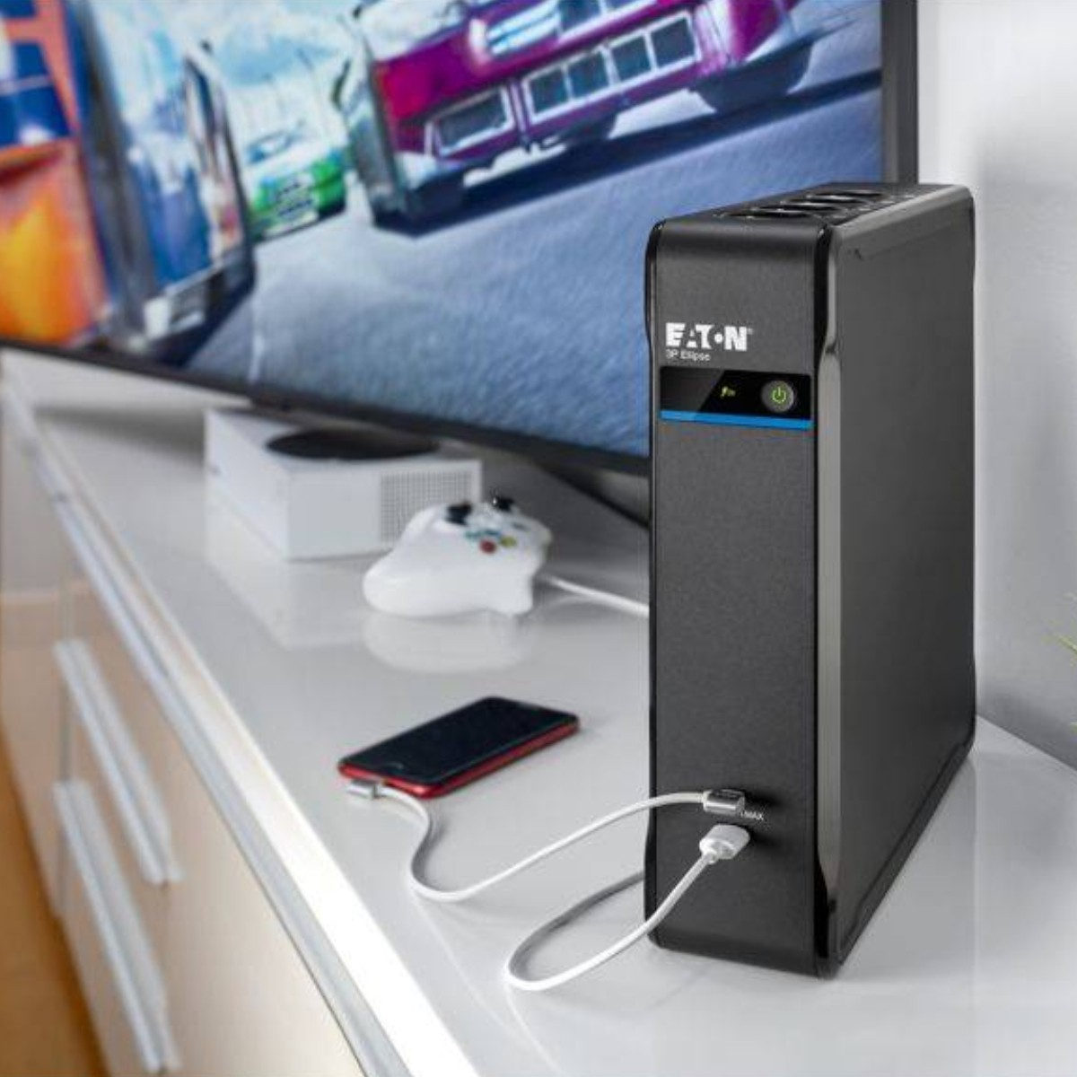 Un UPS Eaton nero carica uno smartphone rosso, con una console di gioco accanto.