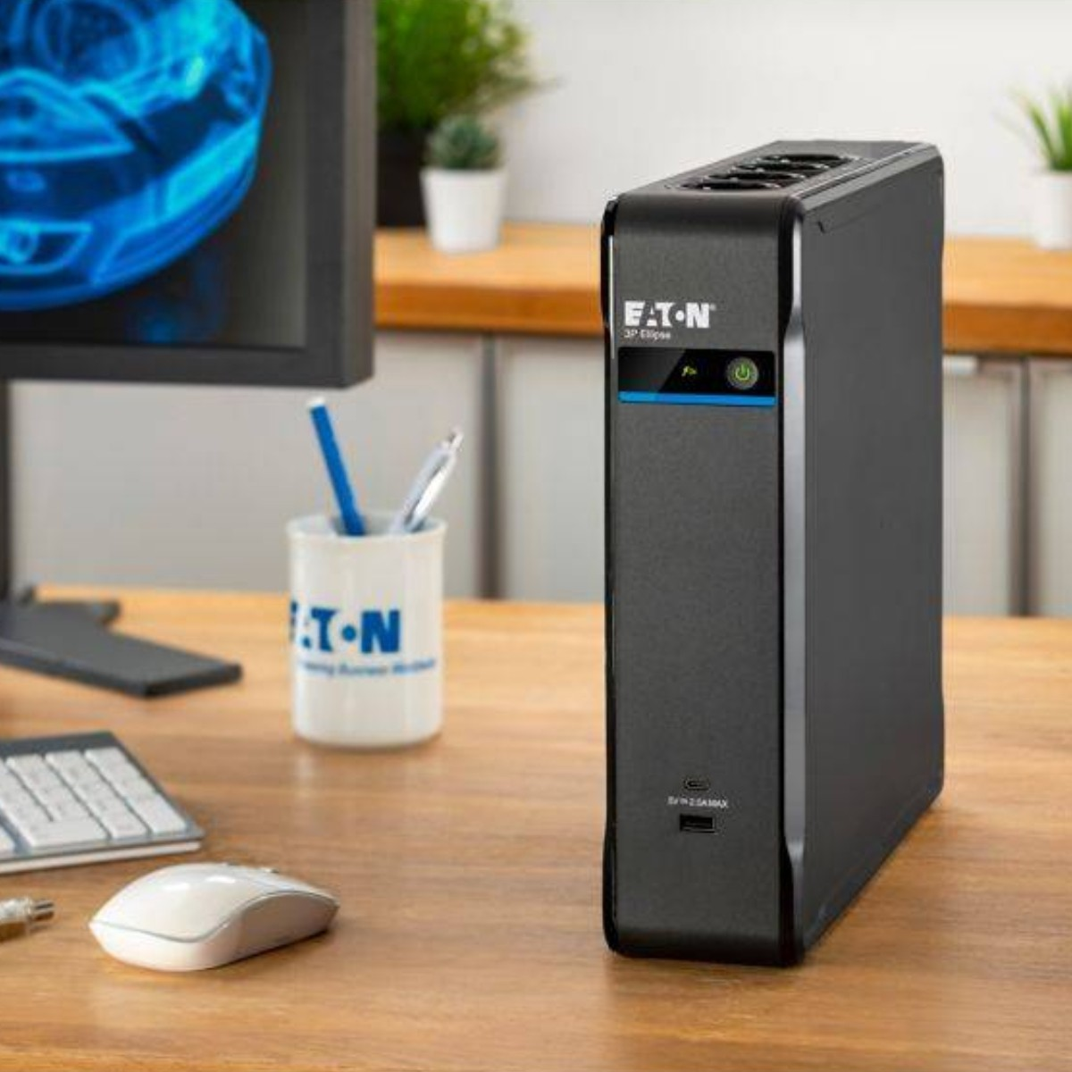 Un gruppo di continuità Eaton nero è su una scrivania di legno accanto a un monitor e un mouse.