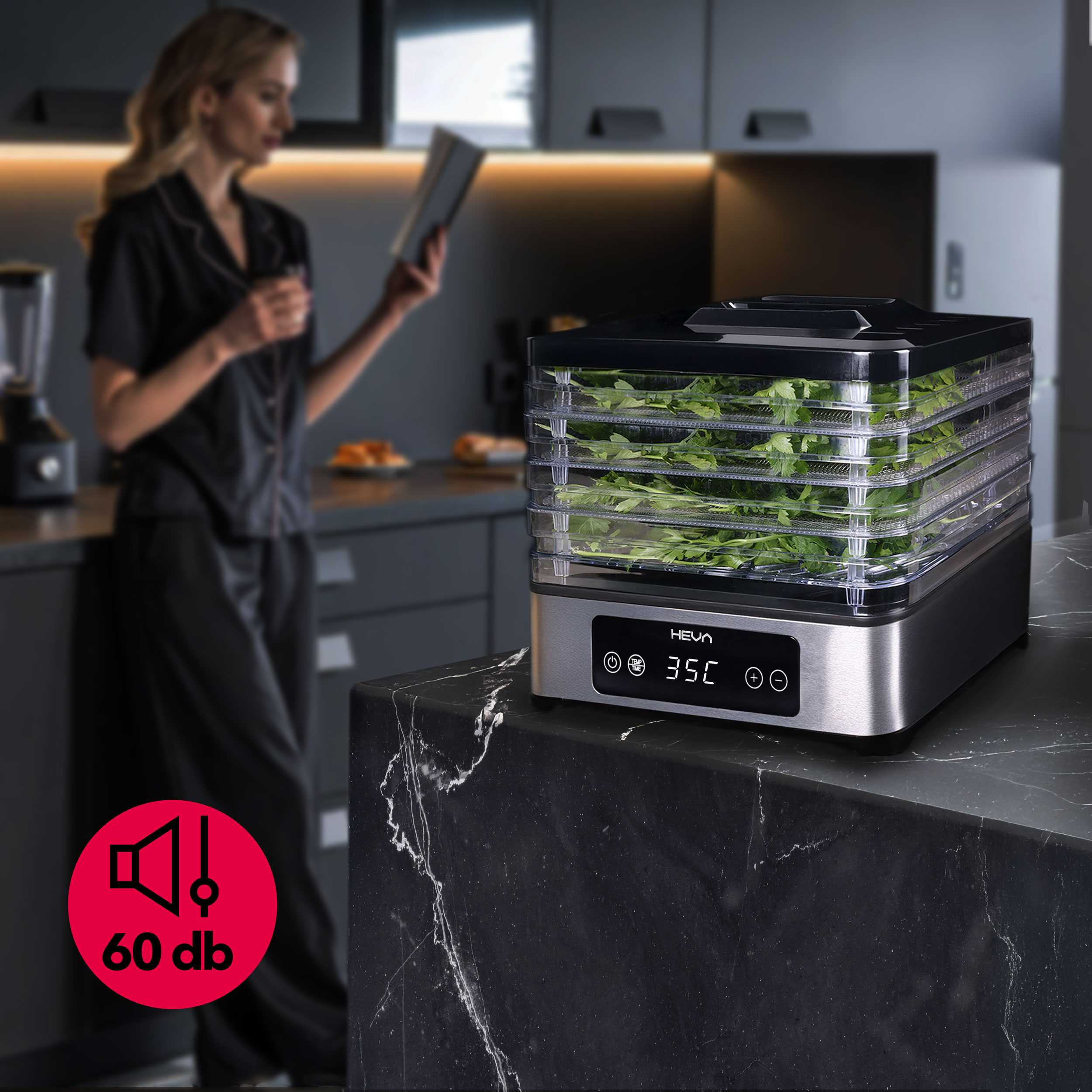 Kobieta czyta książkę obok suszarki do żywności z ziołami i ikoną 60 dB.