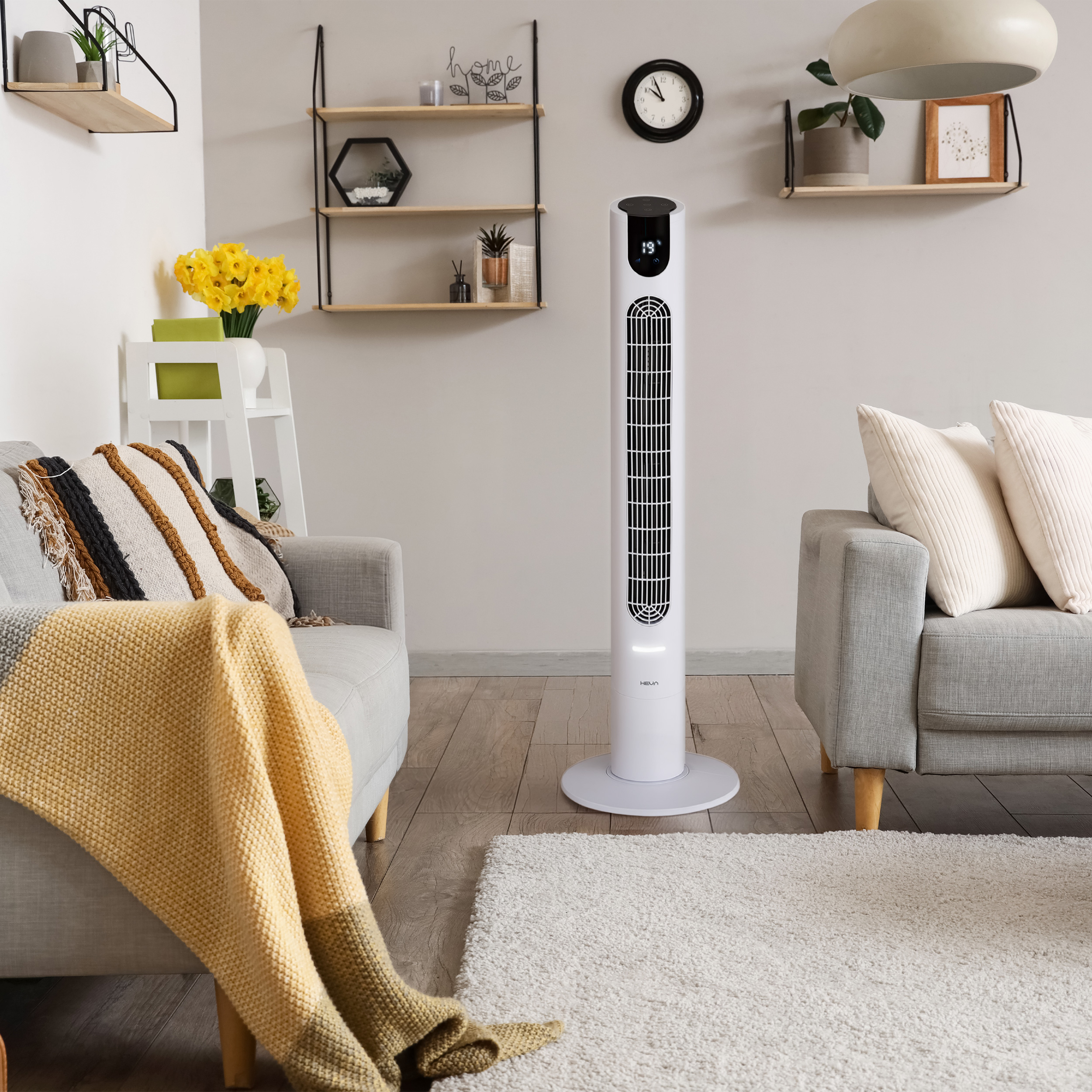 Biały wentylator wieżowy stoi w salonie z dwiema sofami.