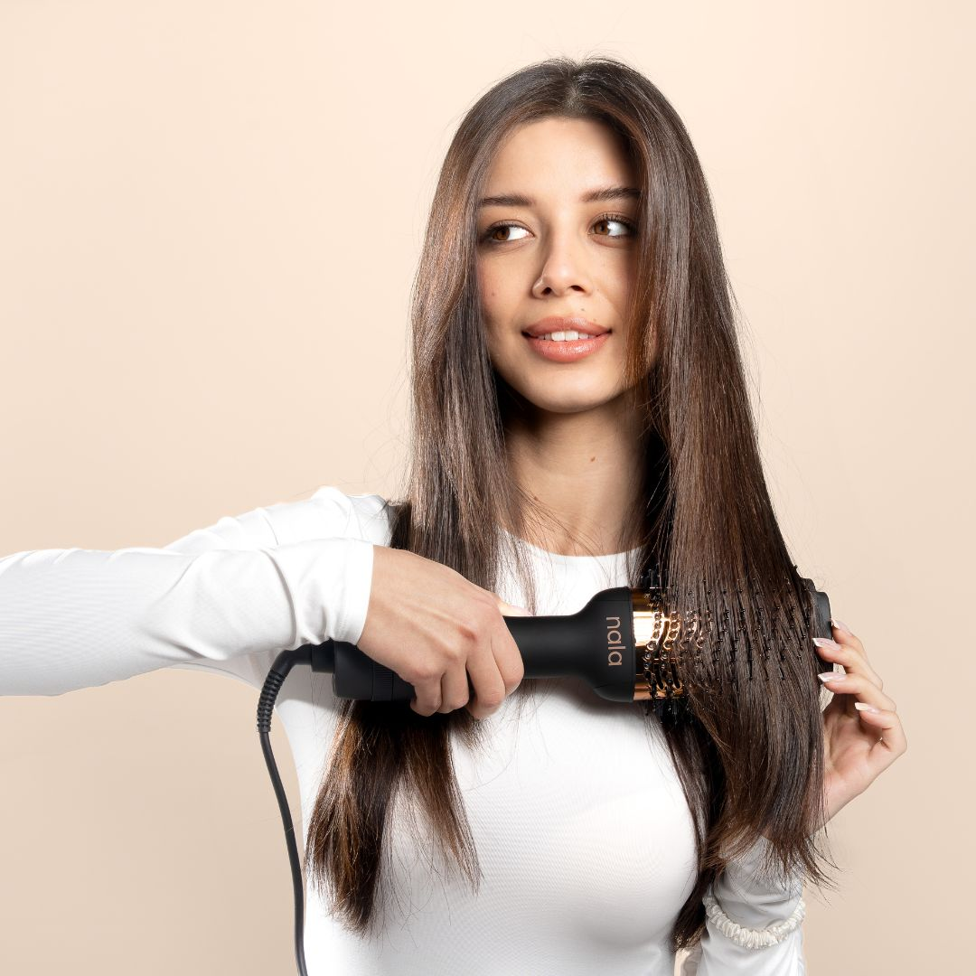 Una donna con lunghi capelli castani usa un arricciacapelli nero sui suoi capelli.