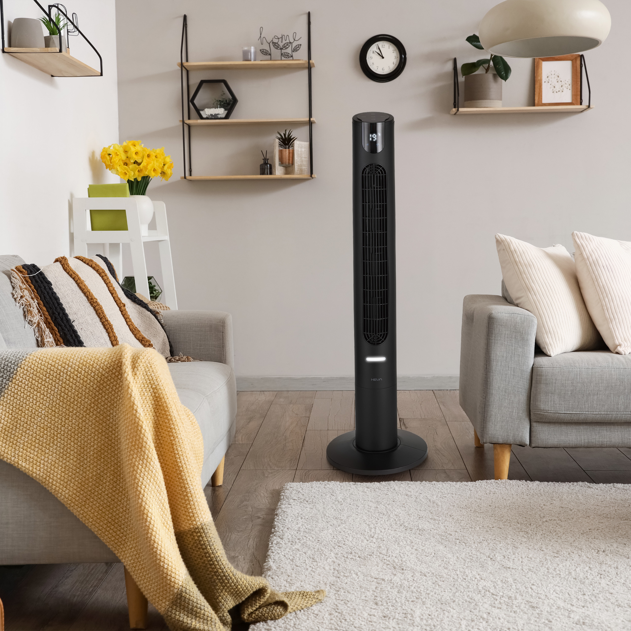 Czarny wentylator wieżowy stoi w salonie obok sofy z poduszkami.