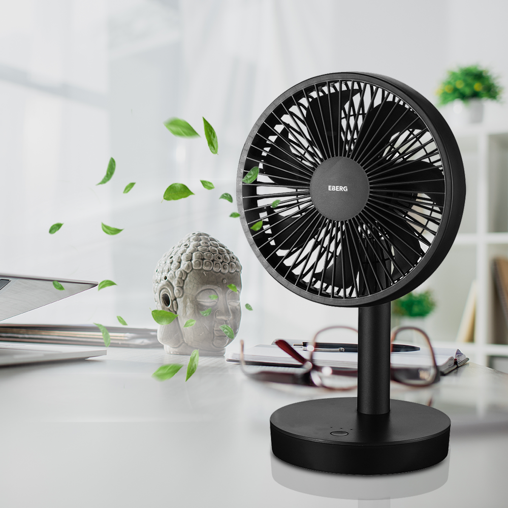 Czarny wentylator na biurku, otoczony poruszającymi się zielonymi liśćmi.