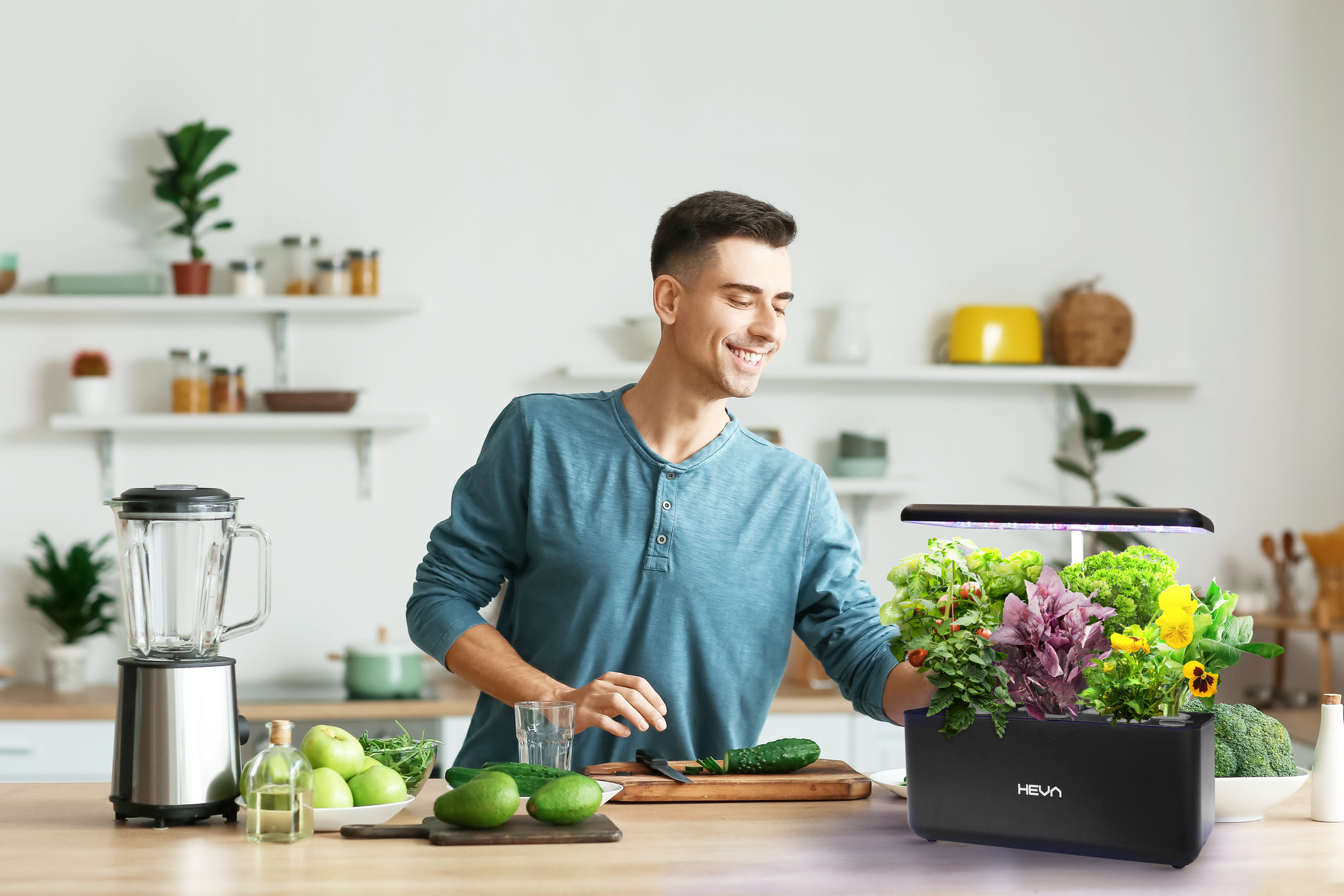Mężczyzna w kuchni pielęgnuje zioła w ogrodzie domowym. Blender, owoce i warzywa na blacie.