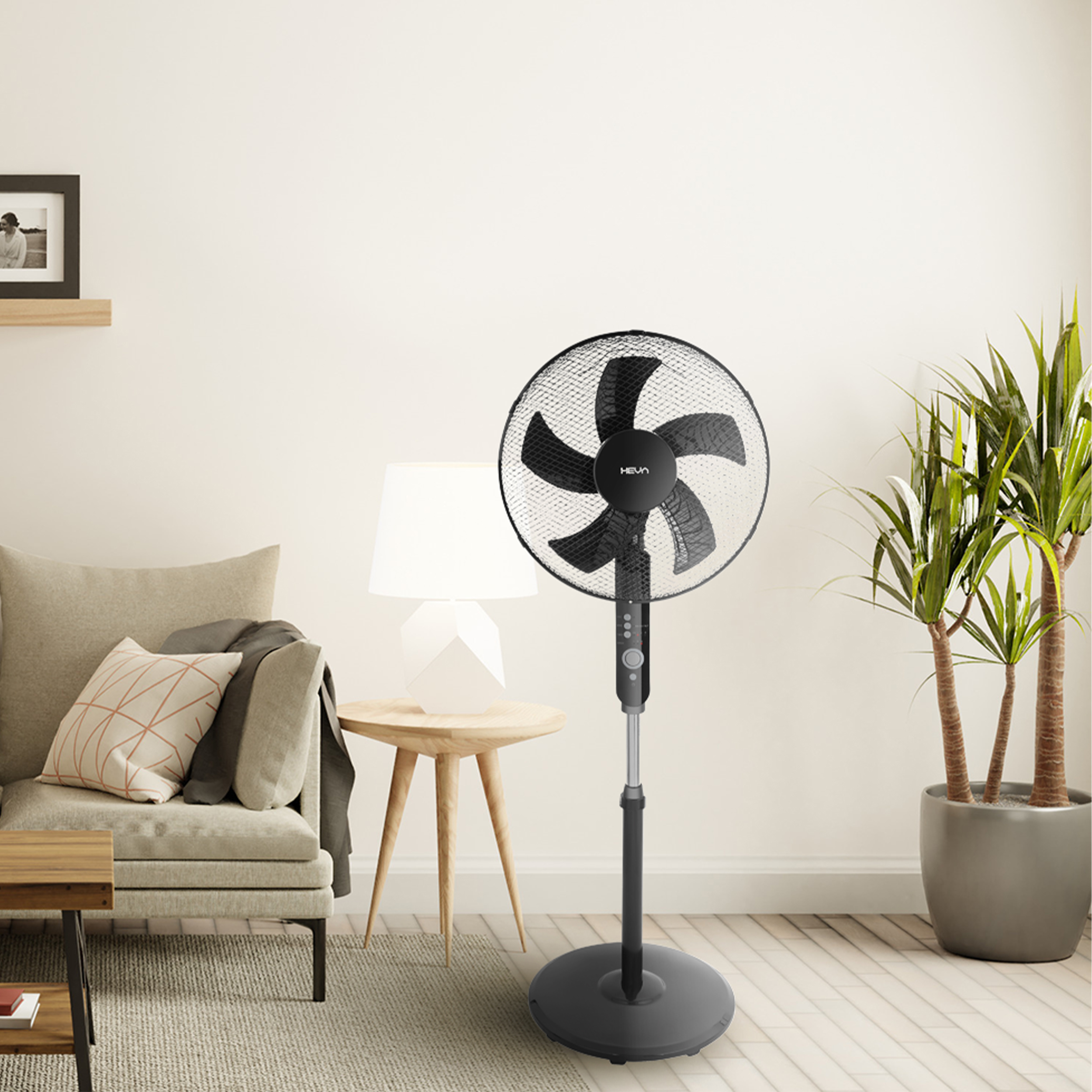 Czarny wentylator stojący stoi obok fotela i stolika bocznego.