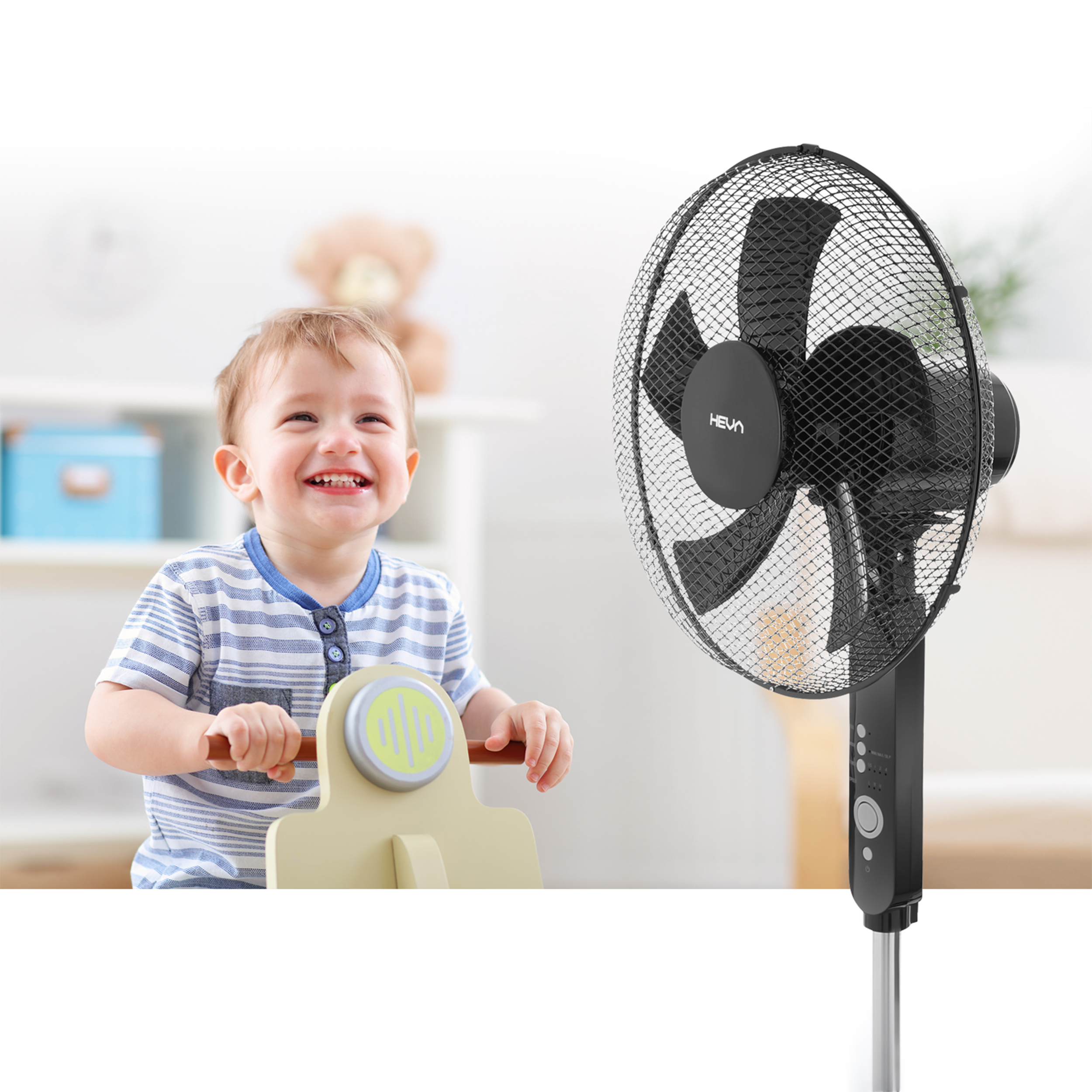 Uśmiechnięty chłopczyk bawi się na drewnianym koniku obok czarnego wentylatora.