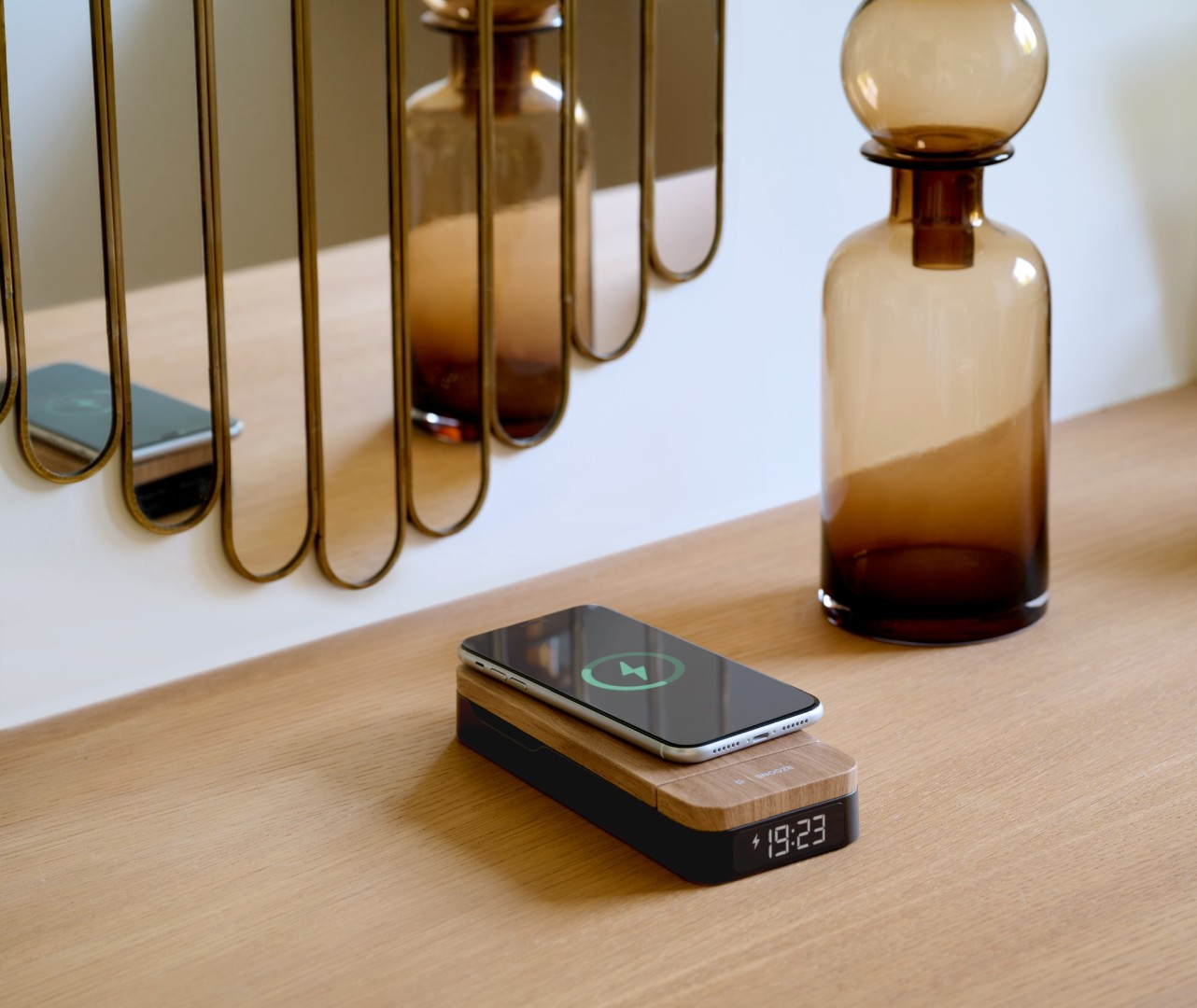 Smartfon ładuje się bezprzewodowo na drewnianej stacji ładującej z cyfrowym zegarem.