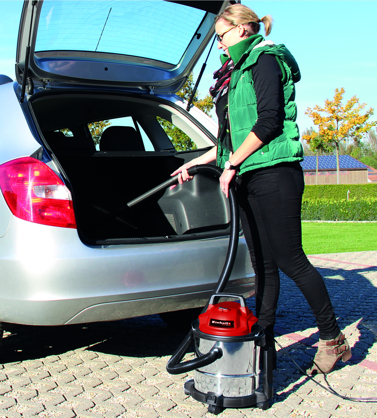 Eine Frau saugt das Auto mit einem roten Nass-/Trockensauger aus.