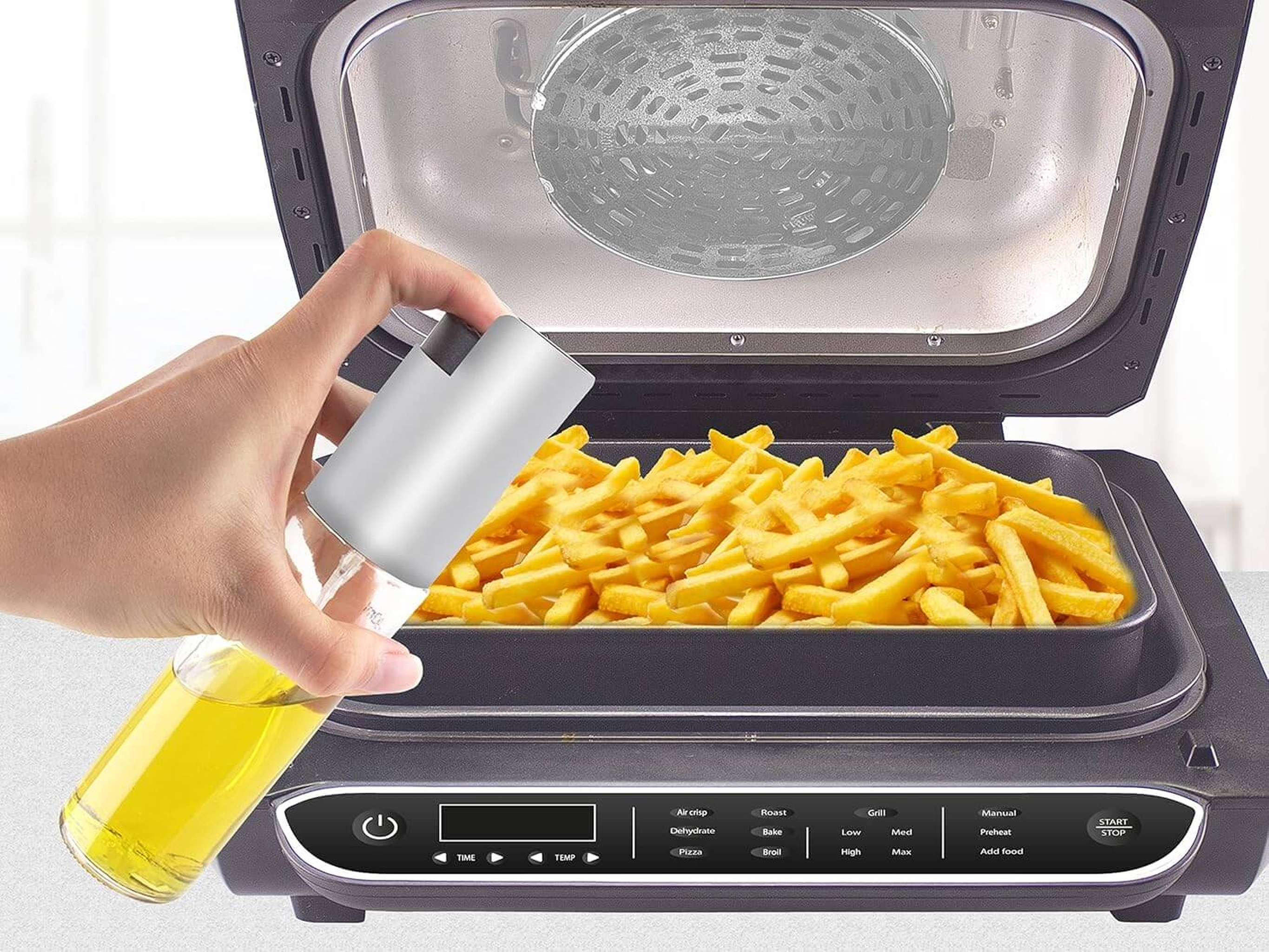 Eine Hand sprüht Öl auf Pommes in einem Heißluftfritteusen-Korb.