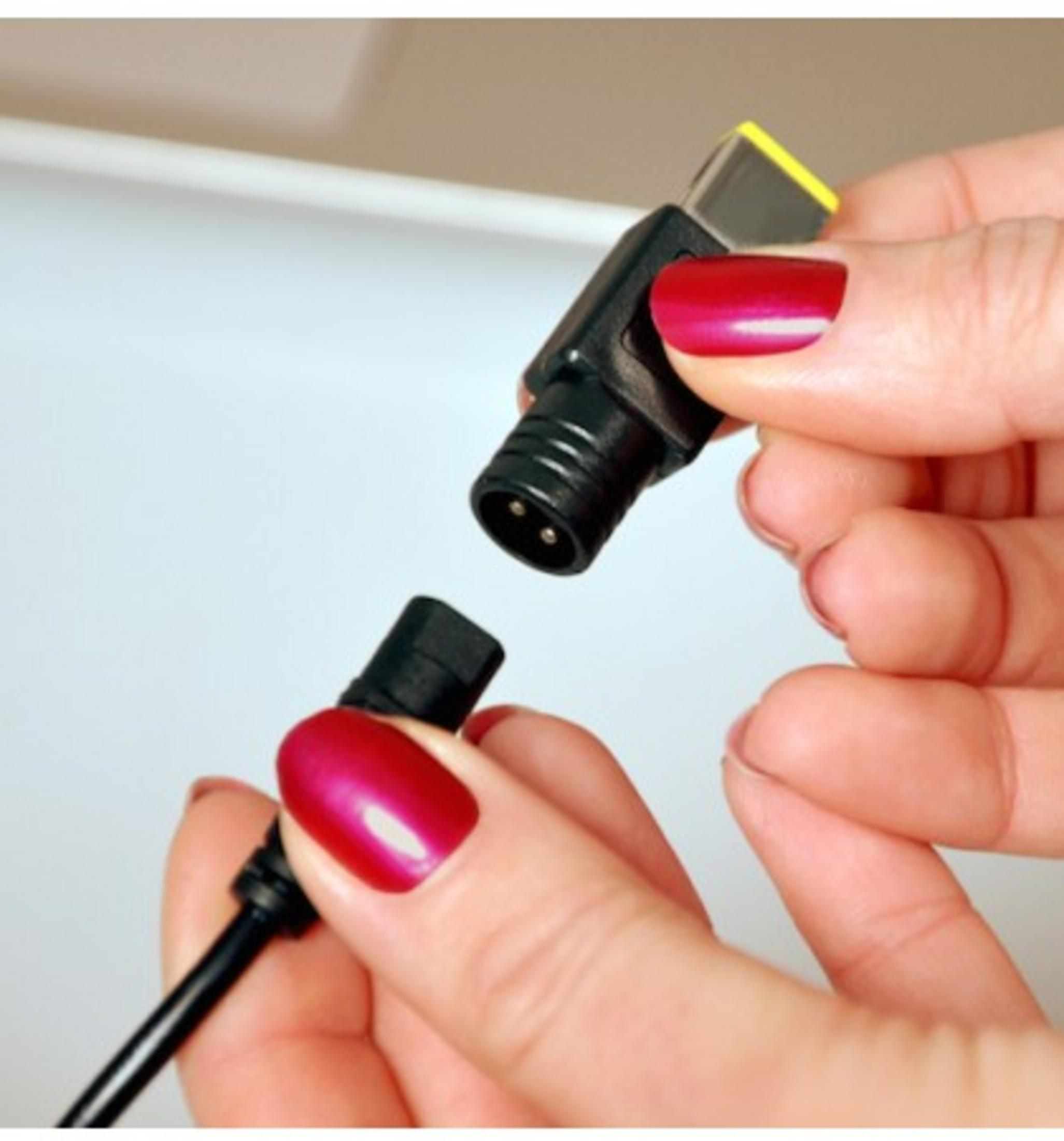 Due mani con unghie rosse collegano un cavo di alimentazione nero a un connettore giallo.