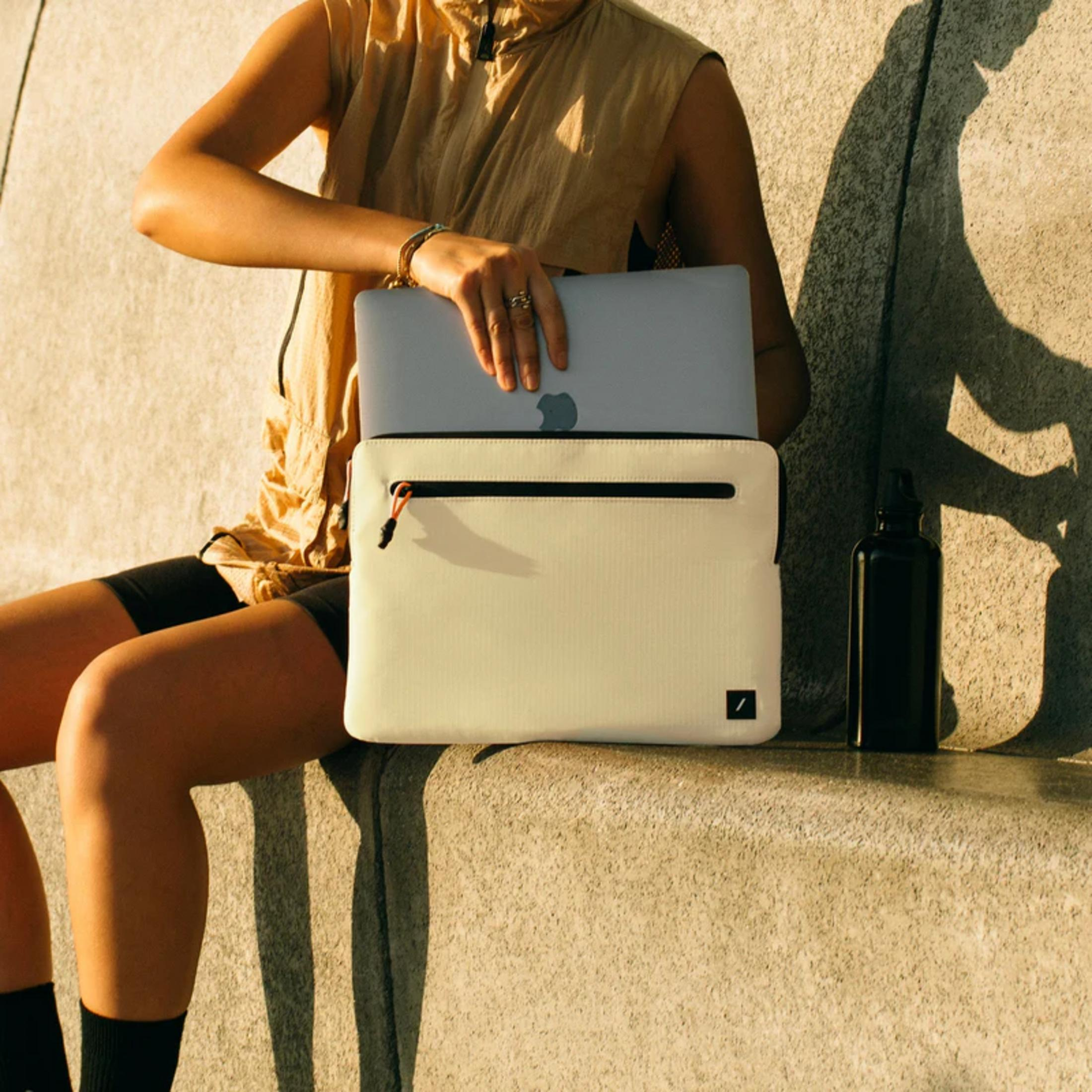 Una persona mette un laptop in una borsa color crema, accanto una bottiglia nera.