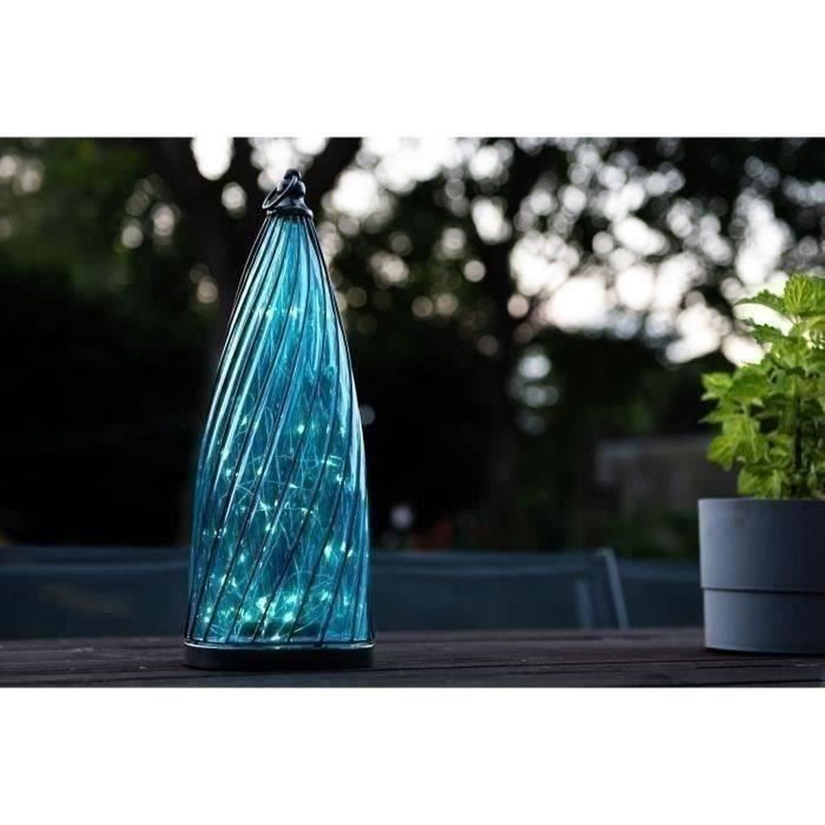 Eine blaue Glaslaterne mit Lichtern auf einem Holztisch im Freien.
