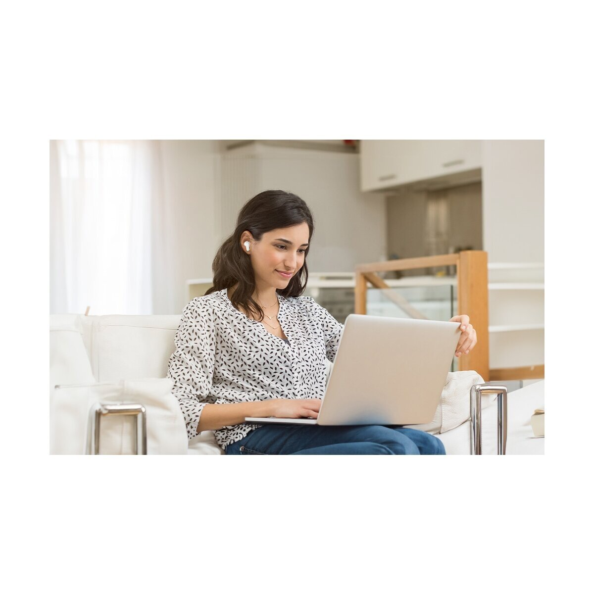 Eine Frau sitzt auf einem Sofa und benutzt einen Laptop. Sie trägt Kopfhörer.